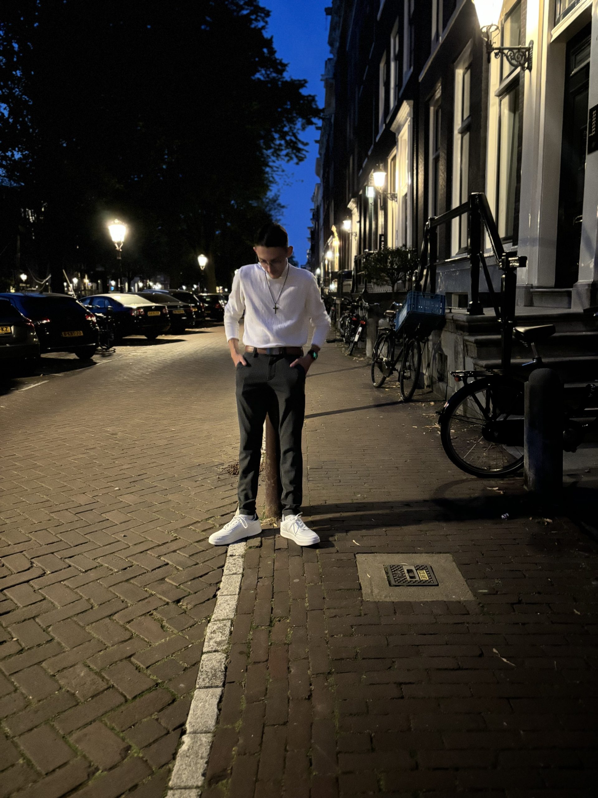 Rapper C2B steht nachts auf einer beleuchteten Straße, trägt ein stilvolles Outfit und blickt nachdenklich zu Boden.